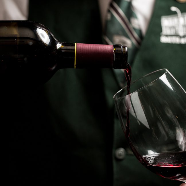 Waiter is pouring red wine into a glass