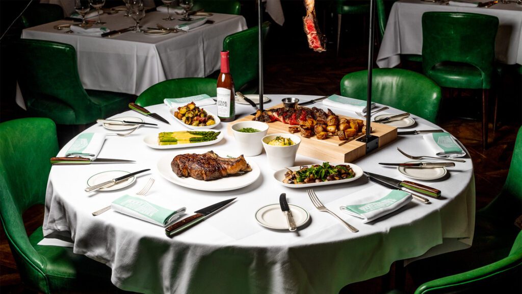 Photo of a table with steak and side dishes surrounded by green chairs