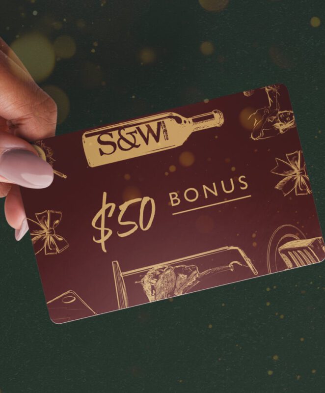 A hand with pale pink nails holds a maroon S&W gift card featuring gold illustrations, a wine bottle logo, and the text 