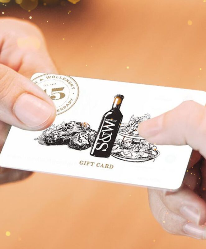 Close-up of two hands exchanging a gift card featuring an illustration of a wine bottle, food dishes, and the text “GIFT CARD” on a white background.