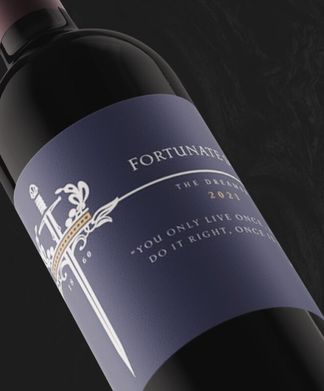 A close-up of a wine bottle with a dark blue label featuring a sword, ornate crown, and text that reads: 