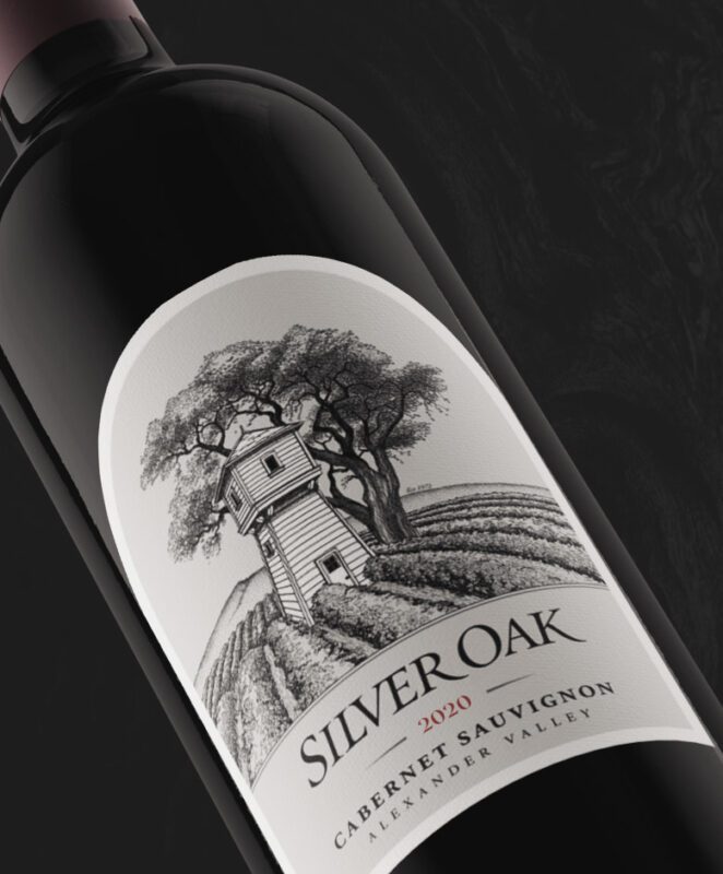 A close-up of a Silver Oak 2020 Cabernet Sauvignon wine bottle, featuring a label with a black-and-white illustration of a wooden tower among vineyards and large trees, and text indicating Alexander Valley.