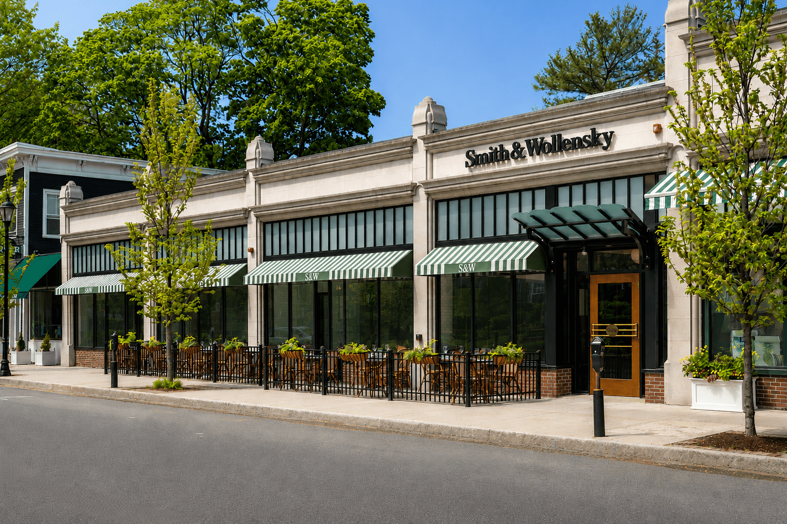 Street view of Smith & Wollensky restaurant with large windows, striped green-and-white awnings, and outdoor patio seating surrounded by planters and young trees on a sunny day.