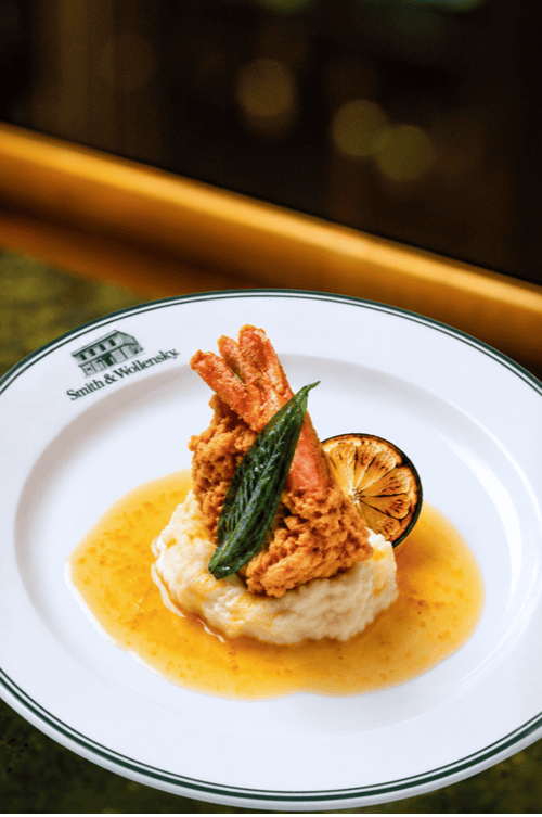 Fried shrimp on mashed potatoes with sauce, garnished with a green herb and a grilled lemon slice, served on a white Smith & Wollensky plate—a perfect addition to the Game Day Menu at Smith & Wollensky Atlantic Wharf. Enjoy this delicious dish while you watch football in Boston.